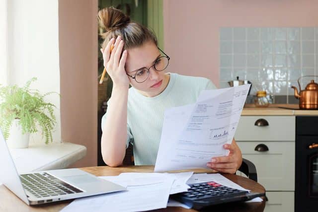 Girl looking at financial documents at home with deeply stressed face looking sick and tired of her economic problems, trying to check counts and all details